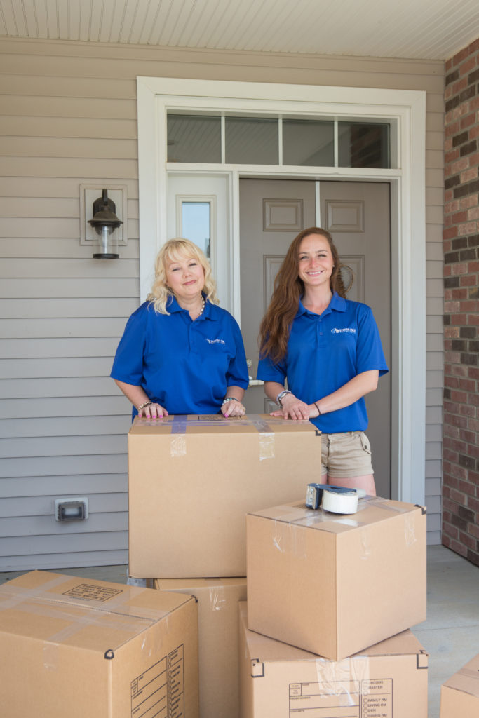 Stress Free Solutions team members standing behind a stack of moving boxes on a client's porch