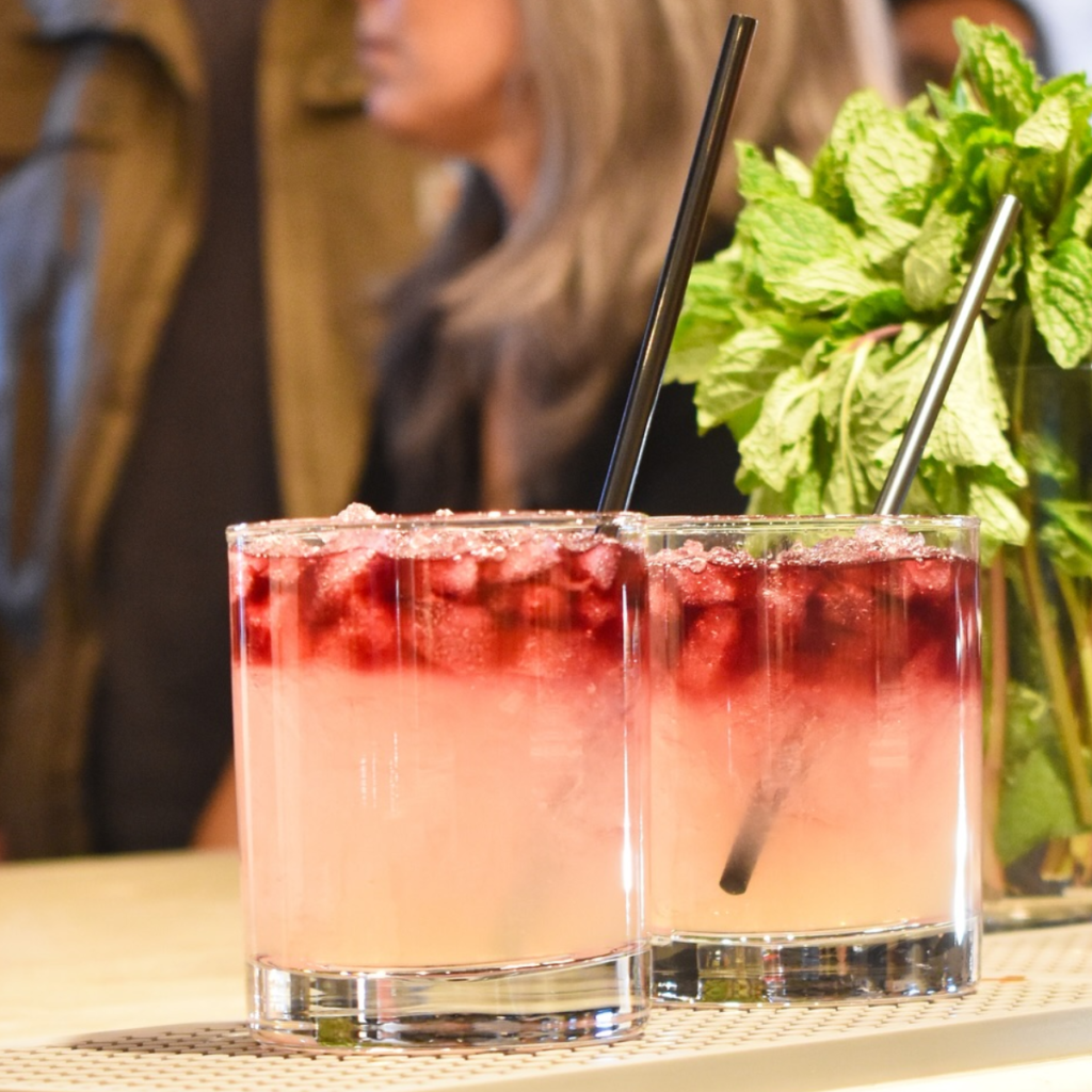 2 cocktails sitting on a bar with fresh mint in a jar behind the cocktails and people in the foreground at True Standard Distilling