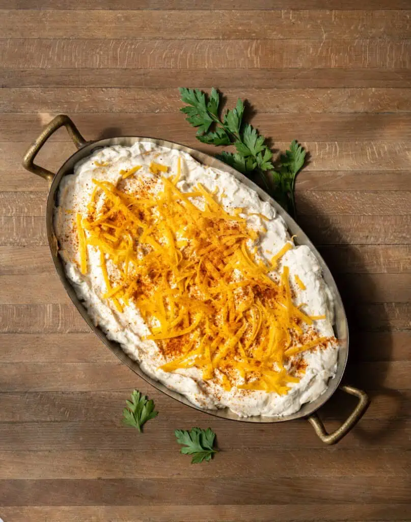Unbaked Maryland hot crab dip topped with shredded cheddar cheese and Old Bay seasoning